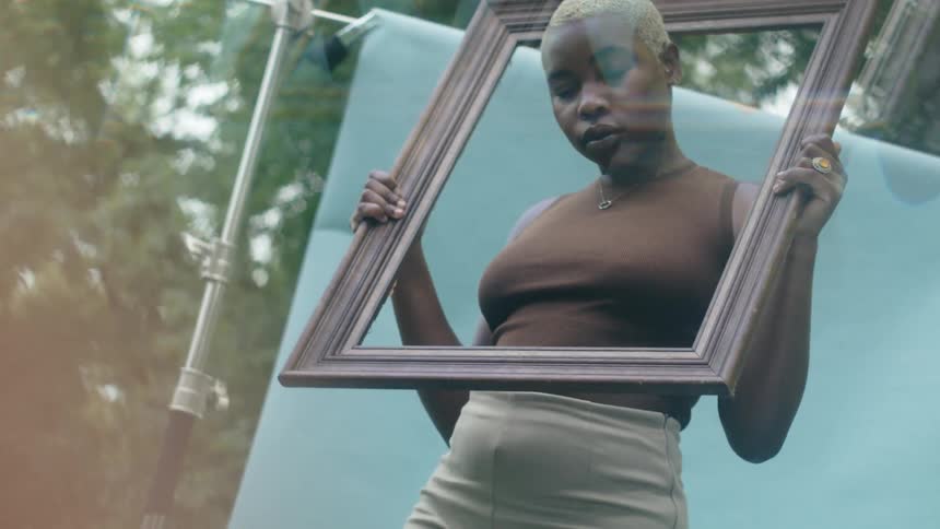 A black woman stands outside and puts a frame over her head