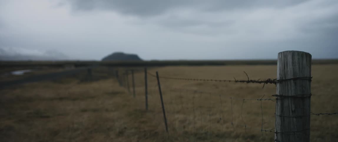 Dark clouds over grass land with a wood post and wire fence