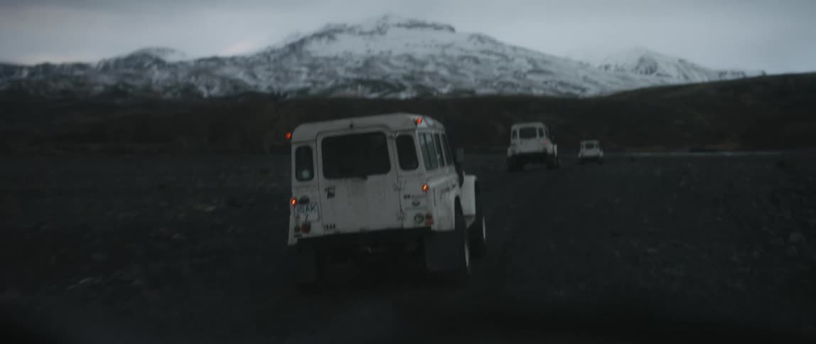 Vehicles drive across a field towards the mountains