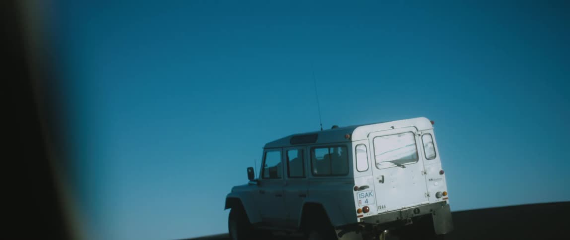A vehicle travels across a barren flatland under a clear blue sky