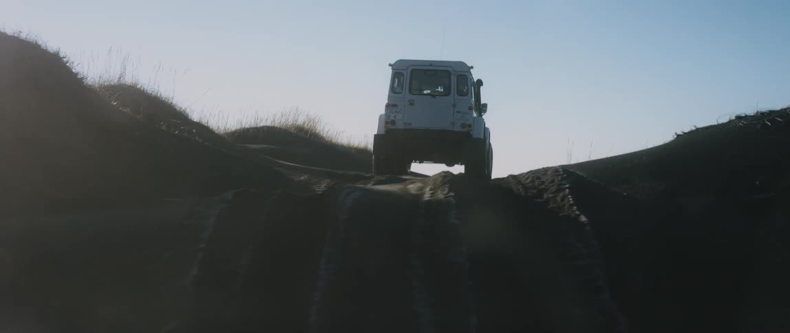A jeep drives through a shallow river and over a steep hill in a canyon