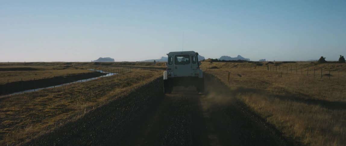 A car is driving on a road in a rural area at sunset