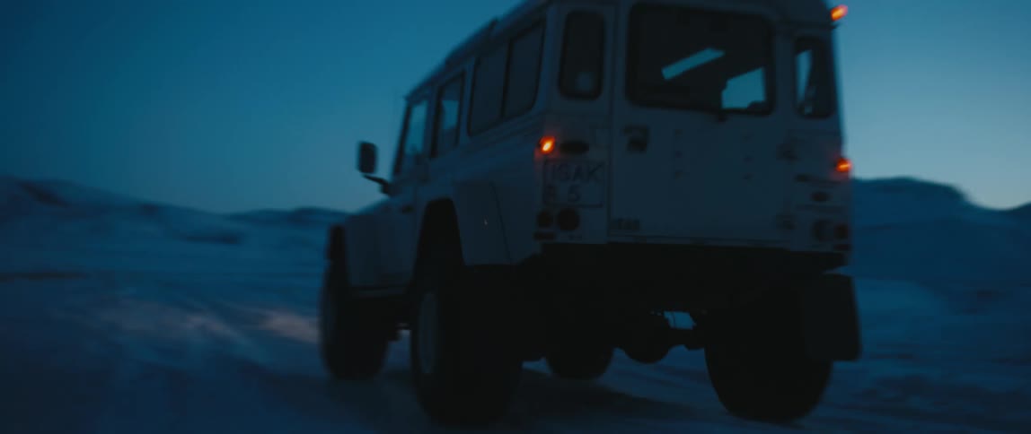 A vehicle travels along a snowy road at dusk