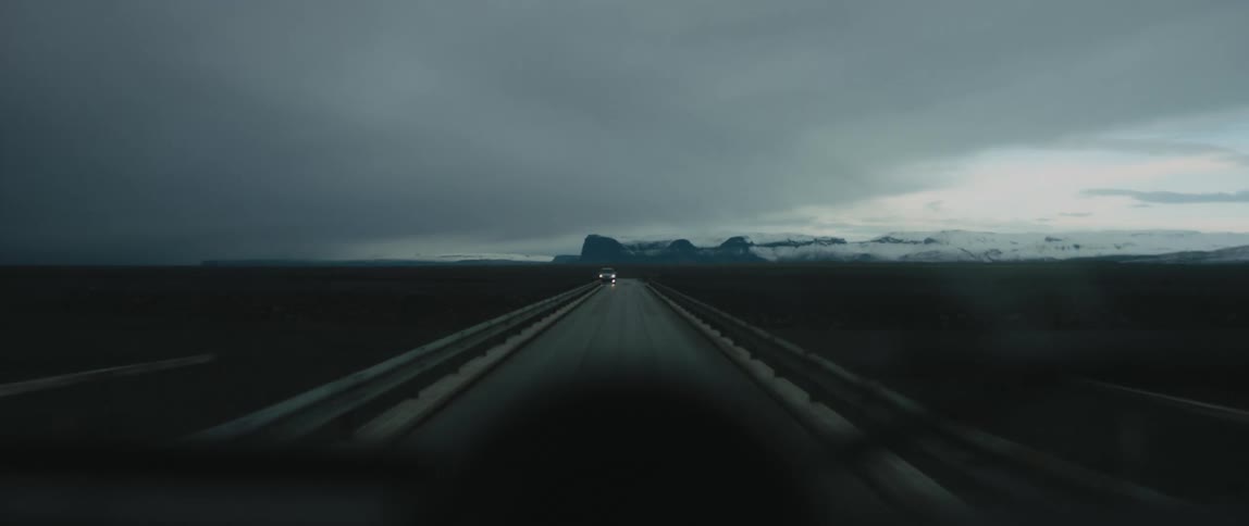 A car drives down a road towards the mountains and passes another vehicle