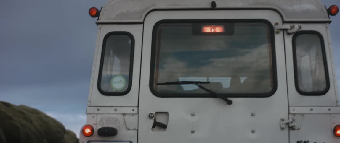 Square vehicle with rear window shied wiper sits parked near rocky mound
