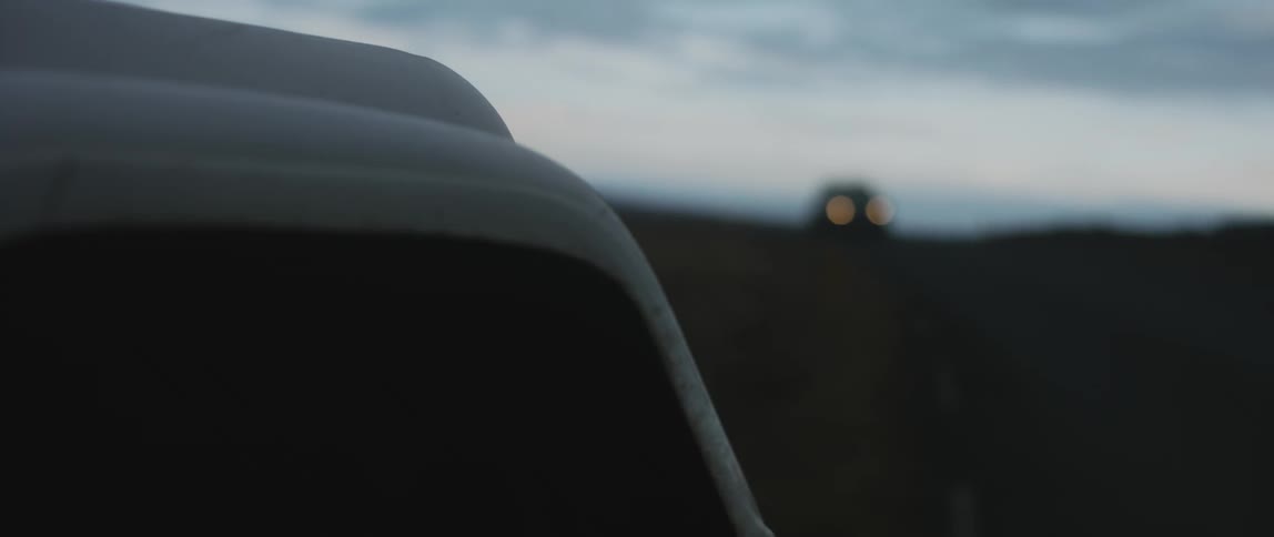 White vehicle sits parked as a car travels past it on the highway