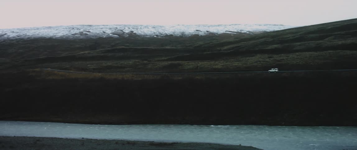 Vehicle travels on a highway between snowy mountains and a lake