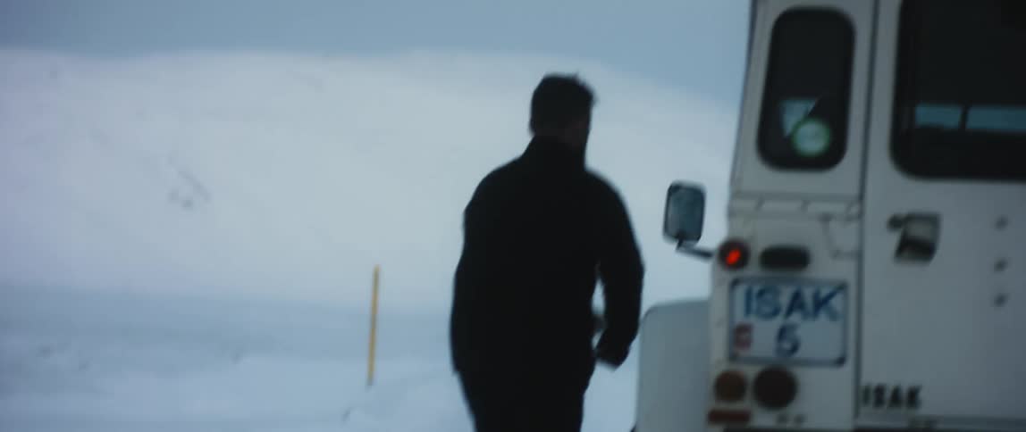 A man walks across snowy ground to enter a vehicle