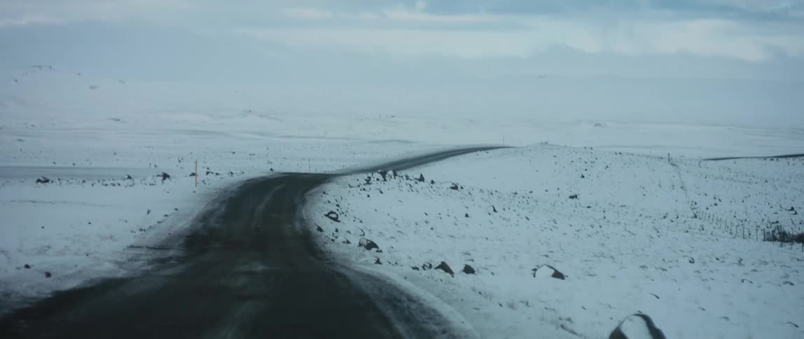 Empty road runs between the snow covered fields under a cloudy sky