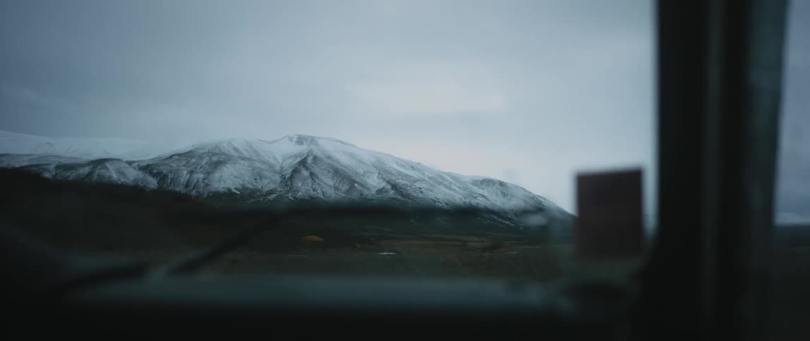A snow covered mountain can be seen in the distance through the windshield of a vehicle