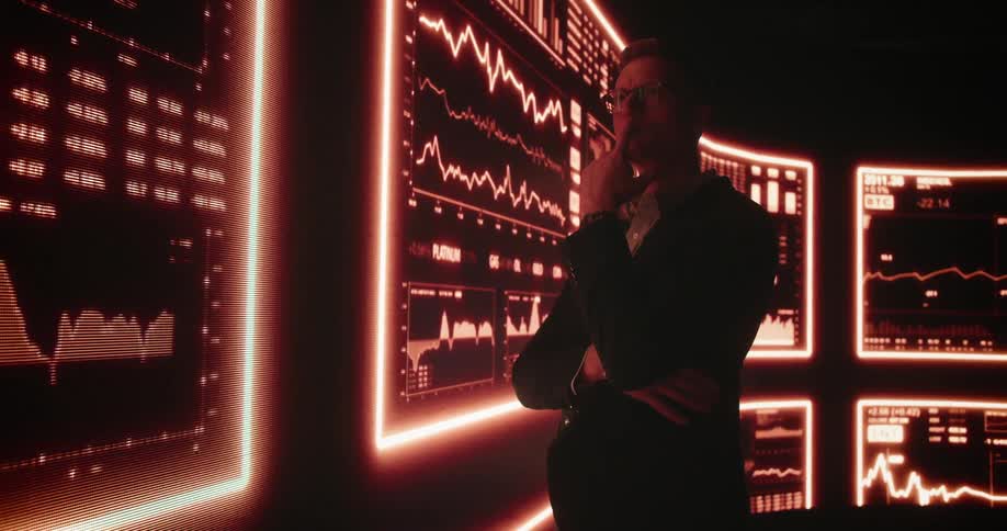 A man stands in a room filled with screens that are all displaying graphs and data