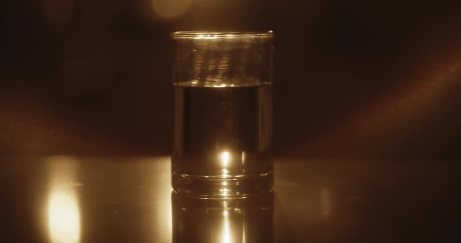 A glass of liquid on a table with light glowing and water surface shimmering