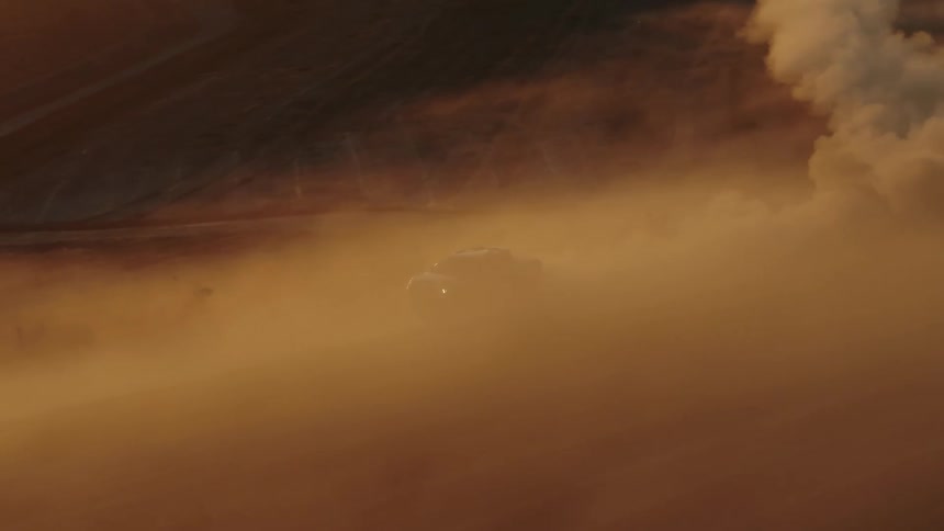 A pickup leaves a trail of dust as it travels on a dirt road past a tractor