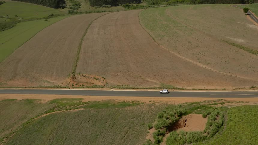 A vehicle drives on a road past farmland