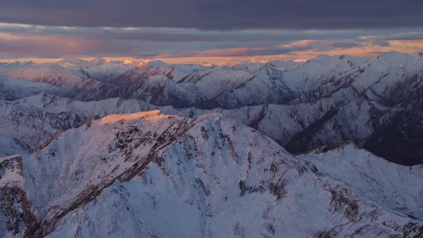Aerial view of the snow covered peaks and slopes of a mountain range at evening