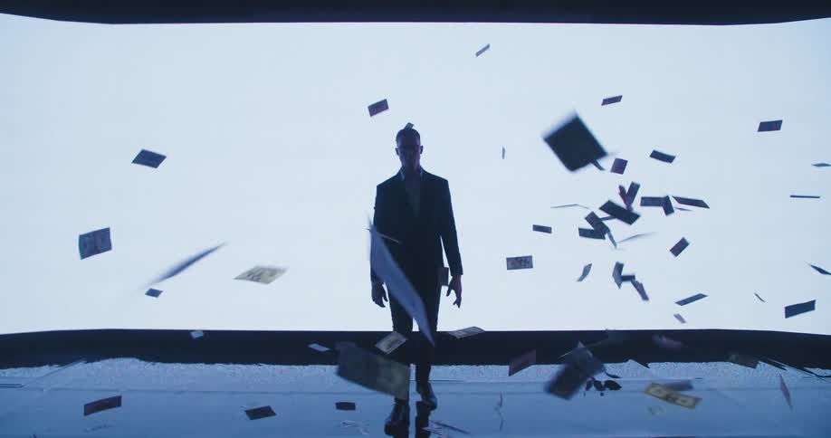 Silhouette of a young businessman walking in front of a large white digital display while dollar bills rain down
