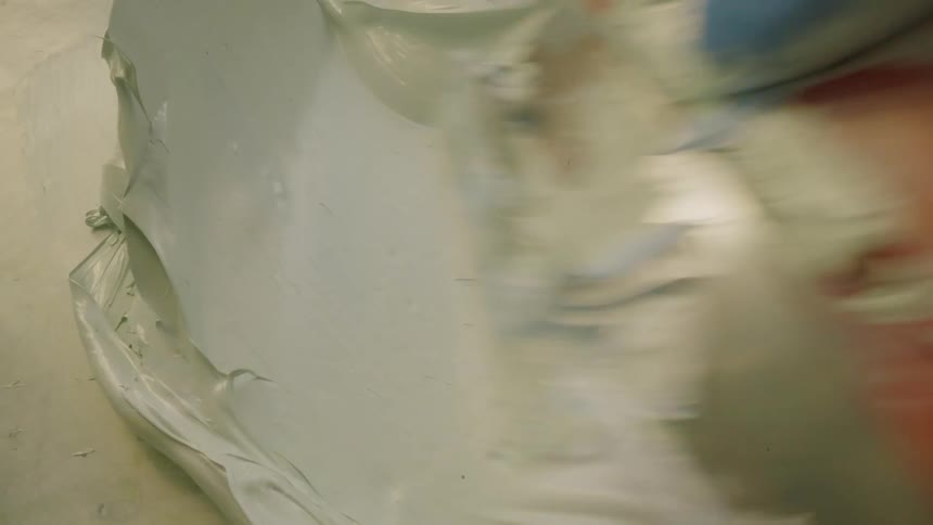Someone is pushing and mixing wet plaster on a flat surface with a scraper