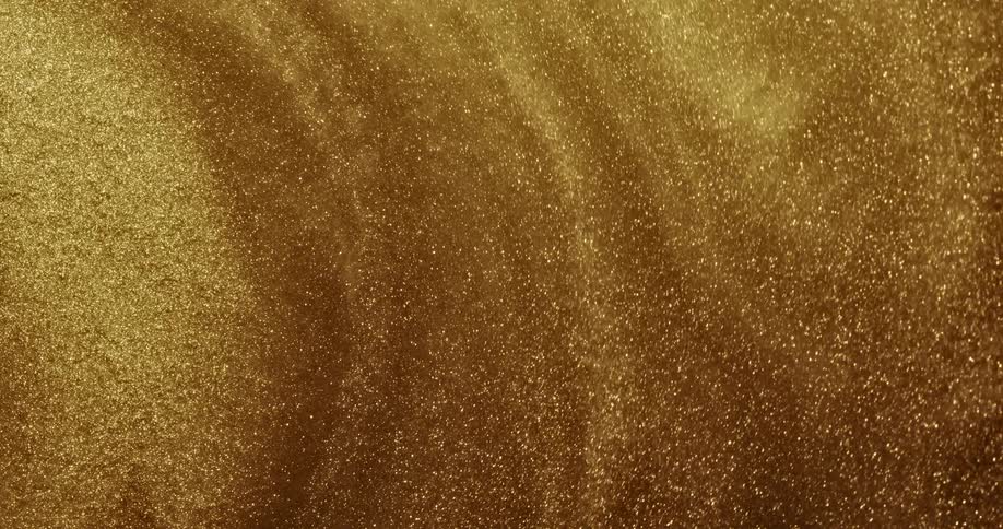 Gold glittery liquid is shown highly magnified swirling around with rippling waves