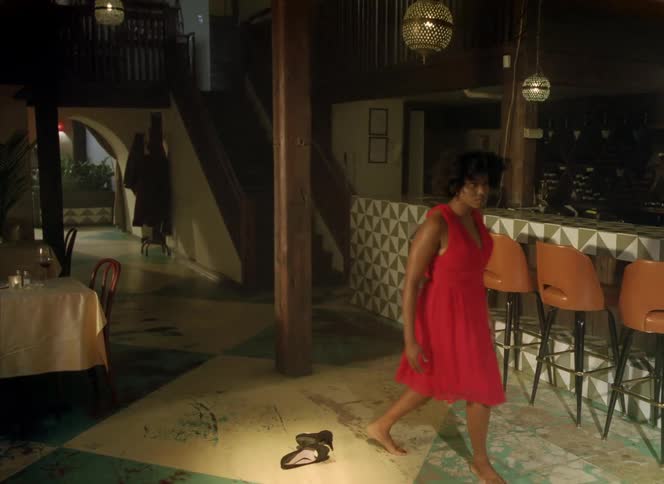 Woman wearing a red dress takes off her high heels shoes and starts dancing on a restaurant