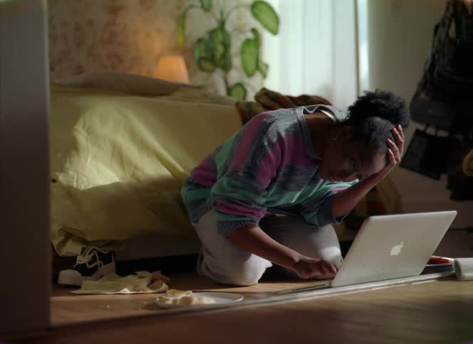 A woman kneeling on a bedroom floor trying to get her laptop to work becomes frustrated