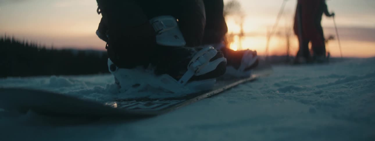 A person clips in to their boots on a snowboard