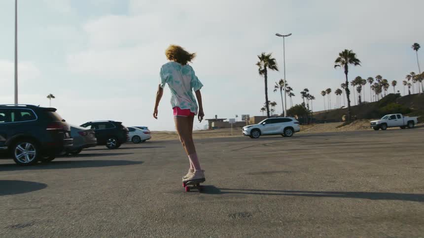 A teenager rides a skateboard through a parking lot