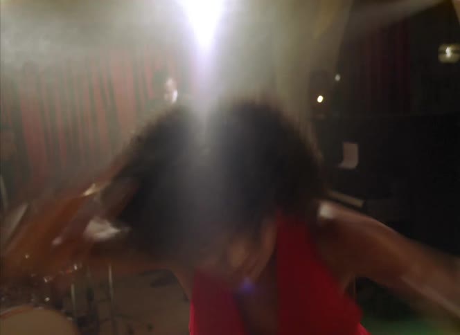 A woman dancing in front of a band playing spins in circles and jumps until she falls to the ground