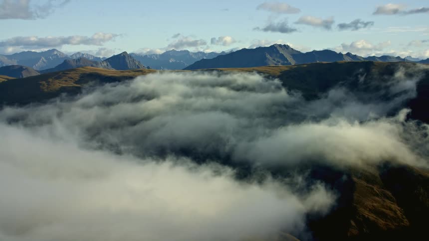 Clouds hang over mountain tops and mountains with peaks high in the sky in the distance