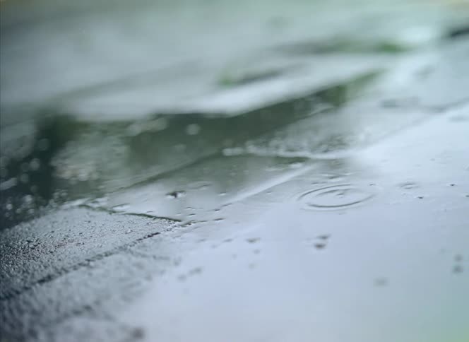 People are walking in the rain as puddles of water are on the walkway