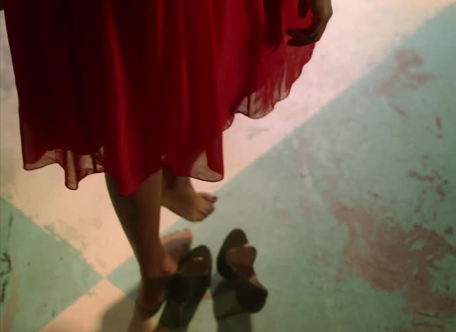 Woman with red dress takes off high heels and walks on stage with drum kit in front of red curtains