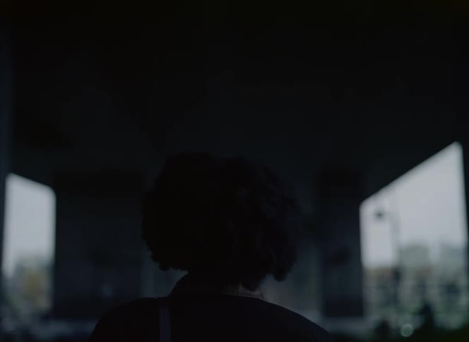 Woman with curly hair and dark top looking around is silhouetted