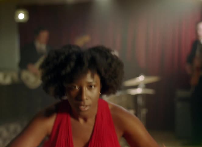 Woman with curly hair and red dress dances in front of band performing in bar