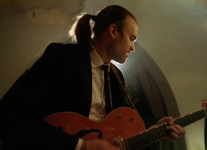 Young musician with a ponytail plays the guitar under a spotlight in a restaurant