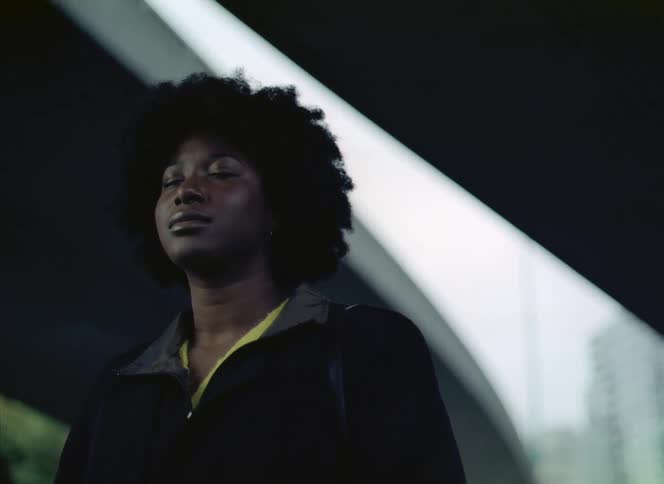 A woman is standing outside as she takes a deep breath and closes her eyes and a bright light flashes