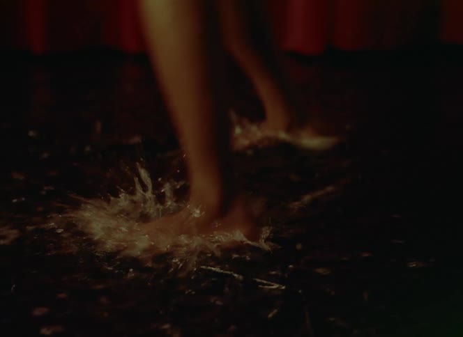 Barefoot woman wearing a red dress dances splashing over a wet floor in front of a red curtain