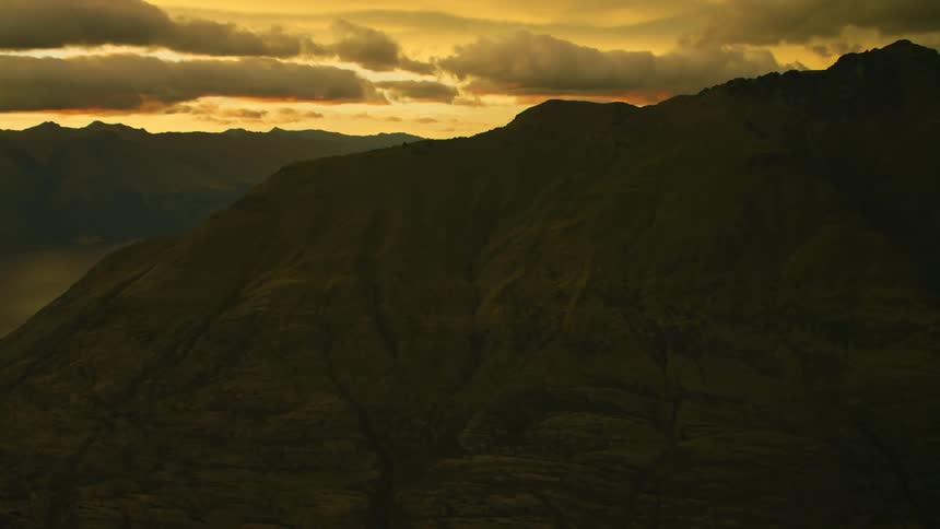 Clouds take on a golden color as sunlight reflects off them over the mountains
