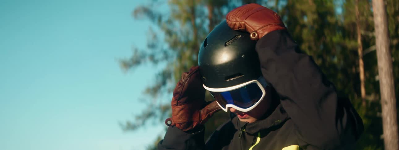 A person adjusts their gloves and helmet while standing outdoors during the day
