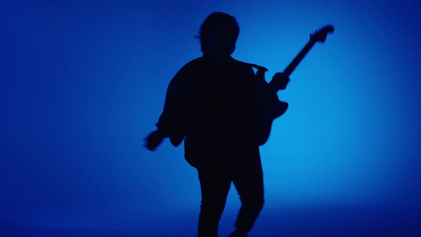 Silhouette of a musician playing electric guitar in front of a blue background