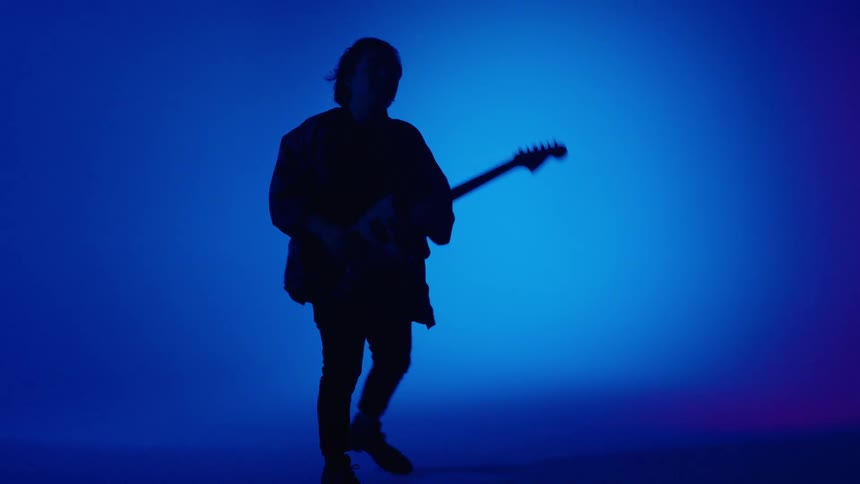 Silhouette of a musician playing electric guitar in front of a colorful background