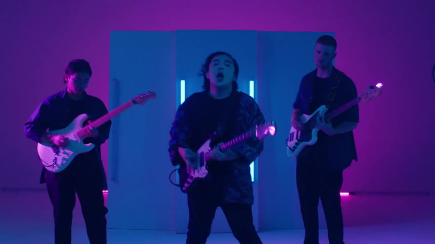 Band of happy excited musicians playing electric guitars and bass on stage under colorful changing lights