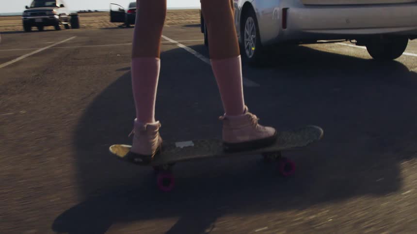 Womans legs with pink socks and white shoes ride skateboard in car park