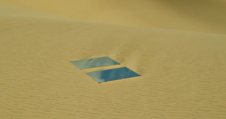 Two large mirrors on a sand dune reflect the blue sky and clouds above
