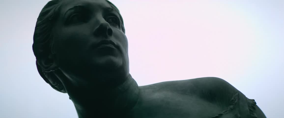 The bust shoulder and face of a female statue against a light blue sky