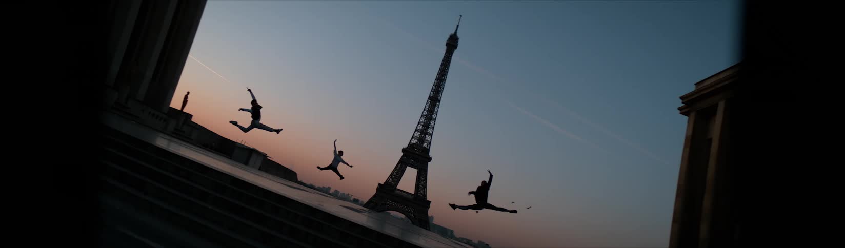 A group of people leap through the air while dancing outside the eiffel tower