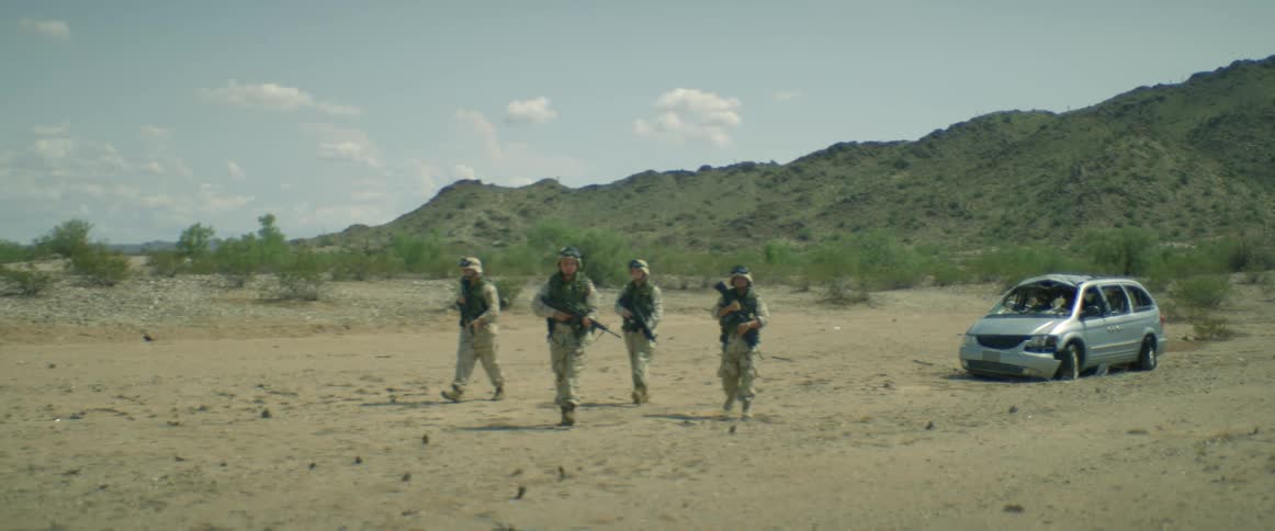 Group of soldiers on a training exercise walking away from a totalled vehicle on a field