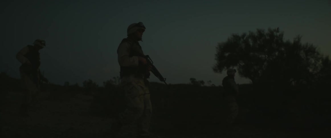 Soldiers with guns are walking across the land in the dark