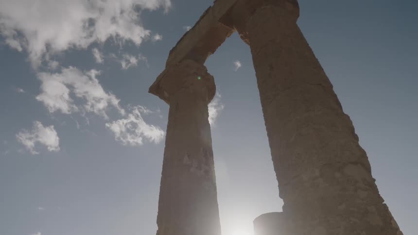 The sun shines behind stone pillars and ruins