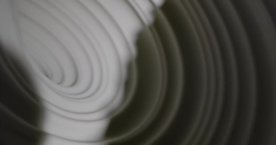 Shadows and light cast over a moving spinning surface of white fabric or porcelain