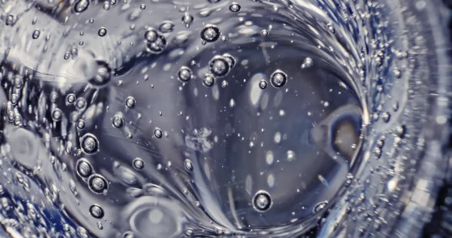 Bubbles rise from a clear liquid that is rippling and moving