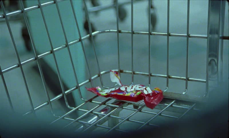 A discarded candy wrapper sits in the bottom of a grocery store shopping cart